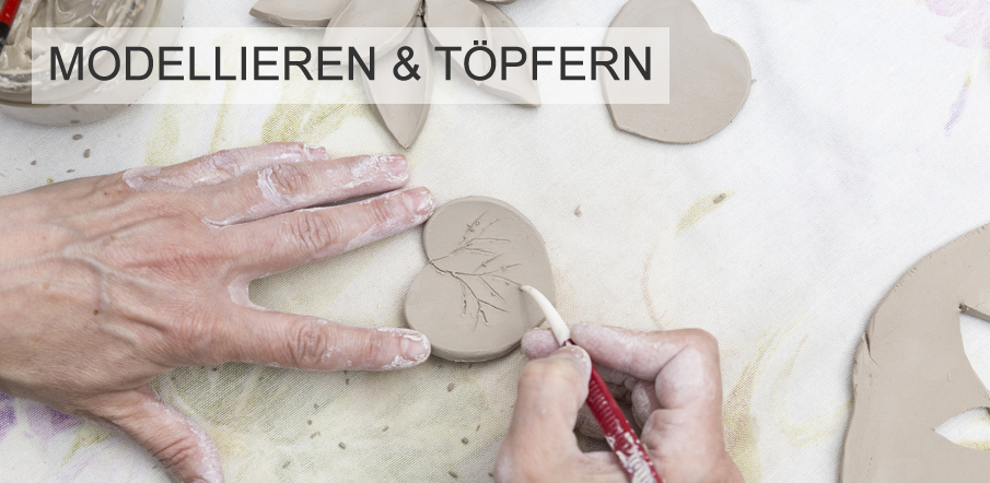 Zwei H�nde bearbeiten Ton: Eine Hand h�lt ein Tonst�ck in Herzform, die andere ritzt mit einem Modellierwerkzeug ein filigranes Astmotiv hinein. Oben im Bild steht der Text 'Modellieren & T�pfern'.